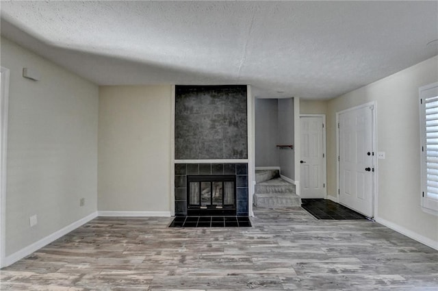 unfurnished living room featuring a tiled fireplace, a textured ceiling, and light hardwood / wood-style flooring