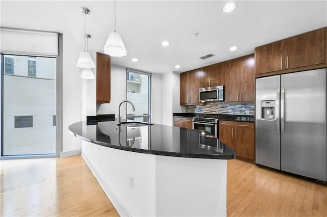 kitchen featuring decorative backsplash, hanging light fixtures, sink, appliances with stainless steel finishes, and light hardwood / wood-style floors