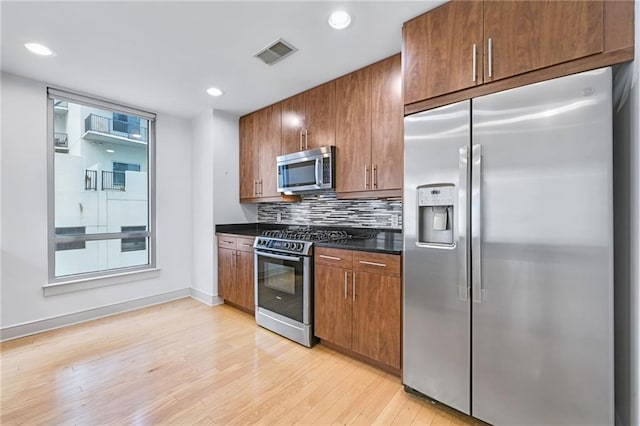 kitchen with backsplash, stainless steel appliances, and light wood-type flooring