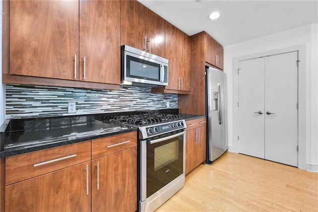 kitchen with decorative backsplash, stainless steel appliances, light wood-type flooring, and dark stone counters