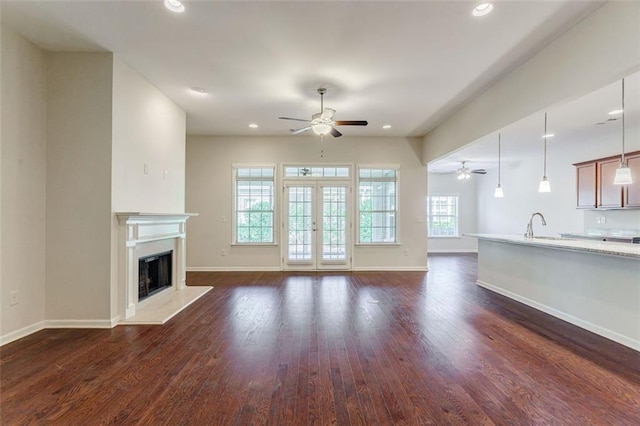 unfurnished living room featuring a ceiling fan, dark wood-type flooring, a fireplace with raised hearth, and baseboards