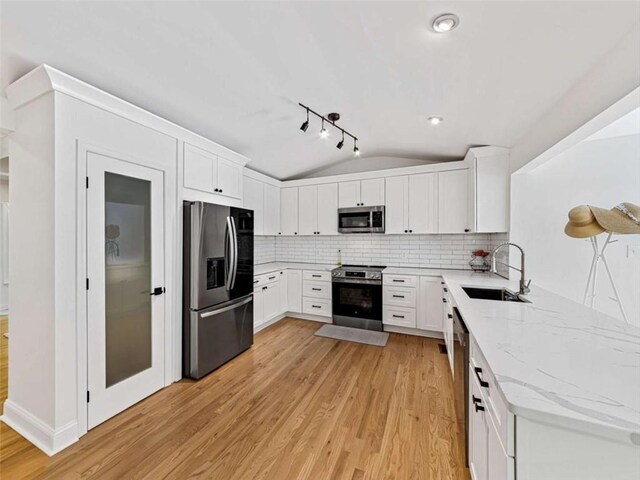 kitchen with a sink, light wood-type flooring, stainless steel appliances, lofted ceiling, and light stone countertops