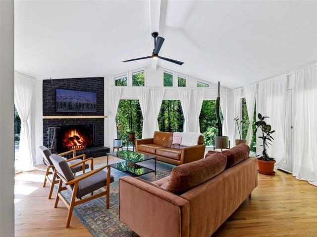 living area with vaulted ceiling with beams, a ceiling fan, a brick fireplace, and light wood-style floors