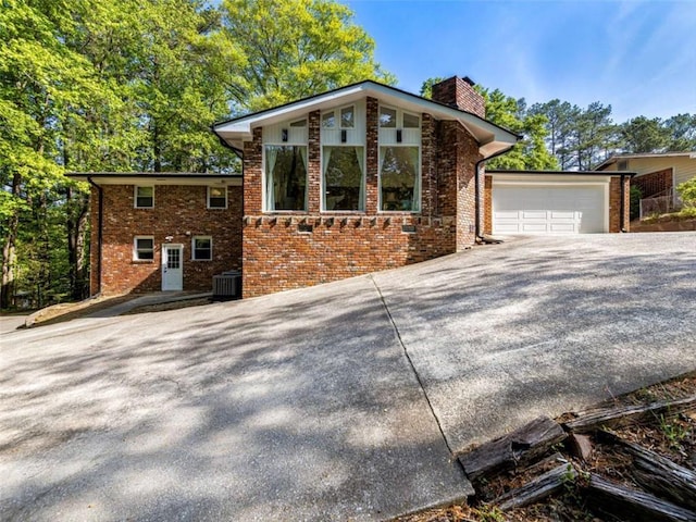 view of front facade featuring a chimney, brick siding, cooling unit, and driveway