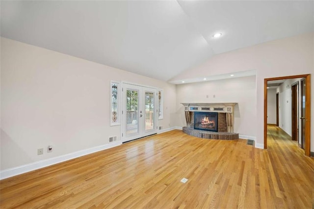 unfurnished living room featuring french doors, light hardwood / wood-style flooring, vaulted ceiling, and a brick fireplace