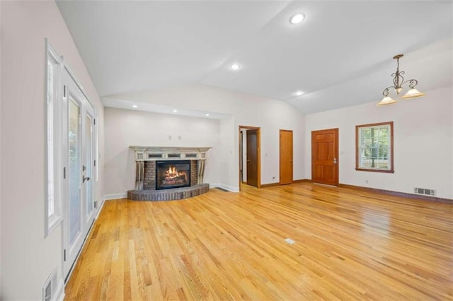 unfurnished living room featuring light hardwood / wood-style floors, lofted ceiling, a notable chandelier, and a brick fireplace