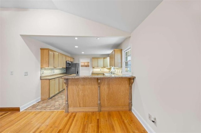 kitchen featuring lofted ceiling, decorative backsplash, kitchen peninsula, light wood-type flooring, and light brown cabinetry