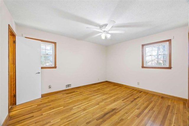 empty room featuring a textured ceiling, a healthy amount of sunlight, light wood-type flooring, and ceiling fan