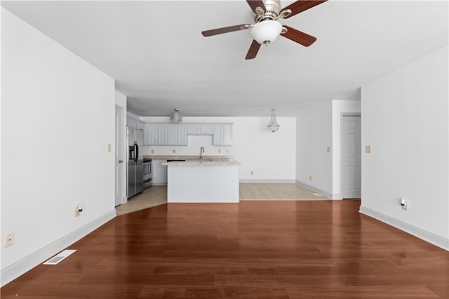 unfurnished living room featuring ceiling fan, sink, and light wood-type flooring