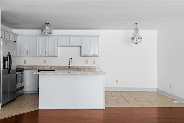 kitchen featuring sink, hanging light fixtures, appliances with stainless steel finishes, light hardwood / wood-style floors, and light stone counters