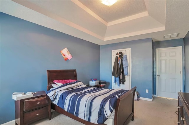 bedroom featuring a raised ceiling, light colored carpet, a textured ceiling, and a closet