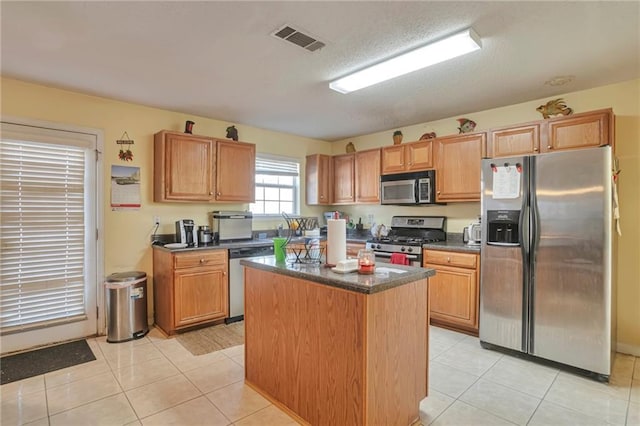 kitchen with a textured ceiling, a center island, stainless steel appliances, and light tile patterned flooring