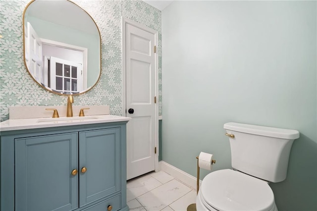 half bathroom with marble finish floor, toilet, vanity, baseboards, and wallpapered walls