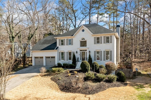 colonial house with concrete driveway, a chimney, roof with shingles, an attached garage, and fence