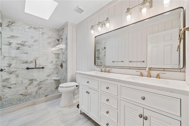 full bathroom with a skylight, a marble finish shower, a sink, and toilet