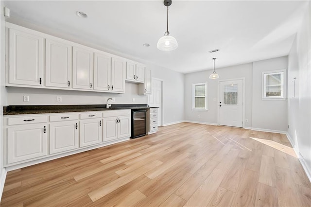 kitchen featuring dark countertops, light wood-style flooring, wine cooler, and white cabinets