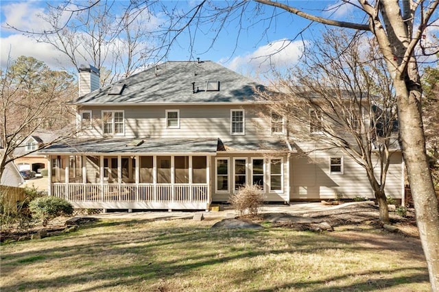 rear view of property featuring a sunroom, a yard, and a chimney