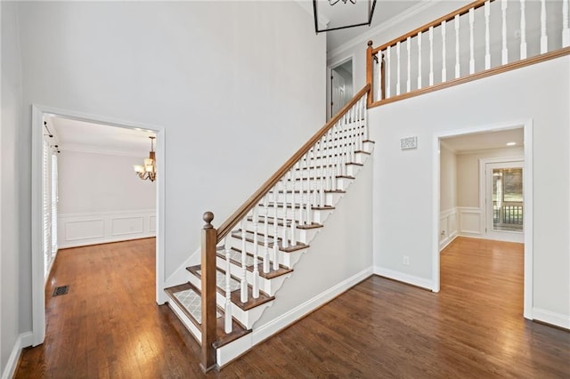 staircase with crown molding, a decorative wall, a high ceiling, wainscoting, and wood finished floors