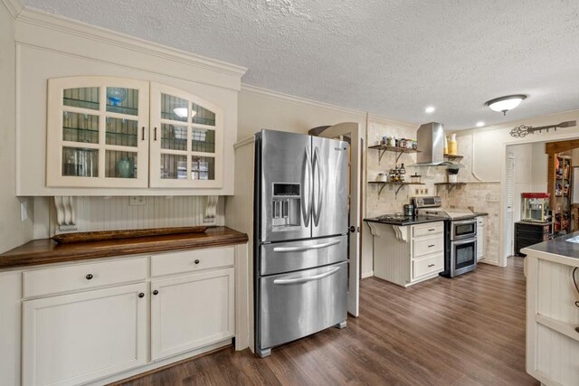 kitchen featuring dark wood-style flooring, crown molding, appliances with stainless steel finishes, glass insert cabinets, and wall chimney exhaust hood