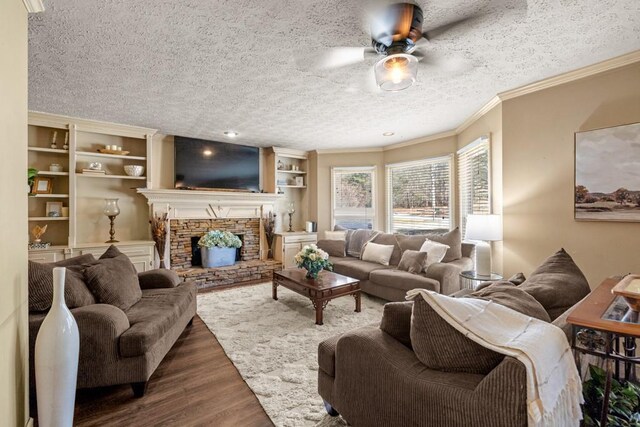 living room featuring a textured ceiling, a stone fireplace, wood finished floors, a ceiling fan, and crown molding