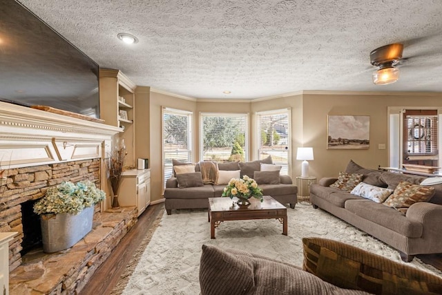 living room featuring a textured ceiling, ornamental molding, wood finished floors, and a stone fireplace