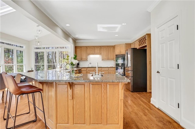 kitchen with light stone countertops, light wood-style floors, crown molding, and freestanding refrigerator