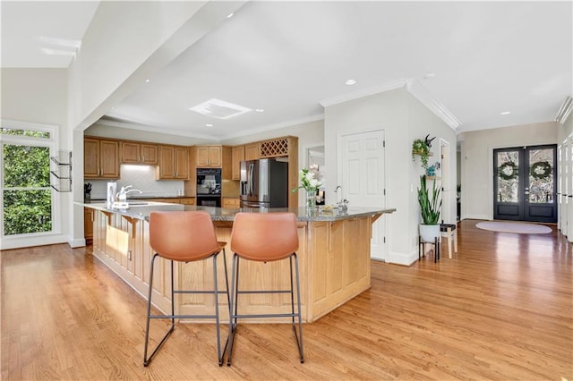 kitchen featuring stainless steel fridge, a breakfast bar, light wood-type flooring, and dobule oven black