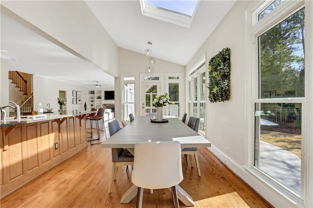 dining area with lofted ceiling with skylight, light wood-style flooring, stairway, baseboards, and ceiling fan