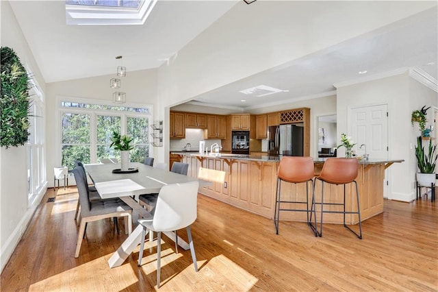 dining area with baseboards, high vaulted ceiling, a skylight, light wood-style floors, and crown molding