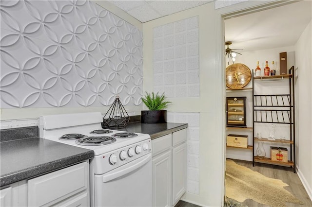 kitchen with dark countertops, a drop ceiling, white electric range oven, wood finished floors, and white cabinetry