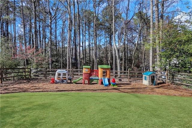 community jungle gym with a lawn, a view of trees, and fence