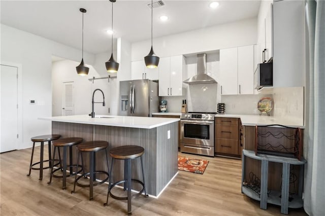 kitchen with visible vents, appliances with stainless steel finishes, a breakfast bar, wall chimney range hood, and a sink