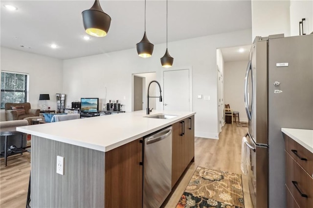 kitchen featuring modern cabinets, stainless steel appliances, light countertops, light wood-type flooring, and a sink