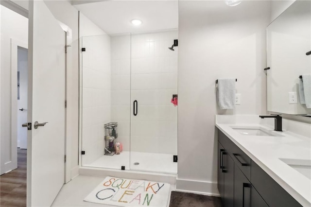 bathroom with double vanity, a shower stall, baseboards, and a sink