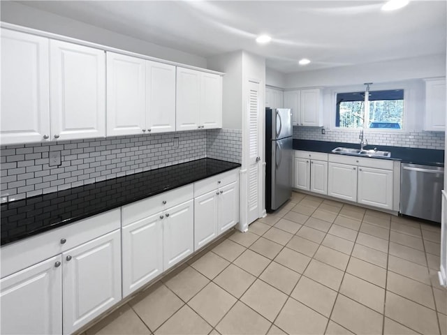 kitchen with light tile patterned floors, a sink, appliances with stainless steel finishes, backsplash, and dark countertops