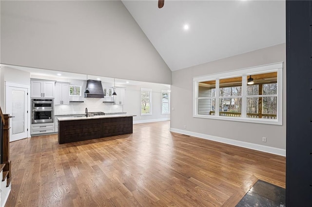 kitchen featuring double oven, light countertops, custom range hood, decorative backsplash, and a sink