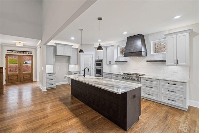 kitchen with backsplash, wood finished floors, stainless steel appliances, light stone countertops, and custom exhaust hood