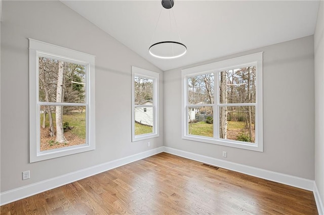 unfurnished dining area featuring vaulted ceiling, wood finished floors, visible vents, and baseboards