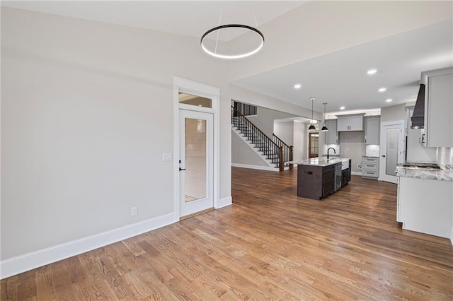 unfurnished living room featuring baseboards, stairway, recessed lighting, wood finished floors, and a sink