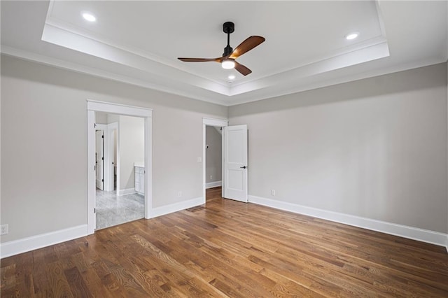 unfurnished bedroom with ornamental molding, baseboards, a tray ceiling, and wood finished floors