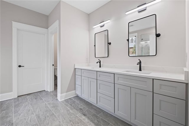 bathroom with a sink, baseboards, toilet, and double vanity