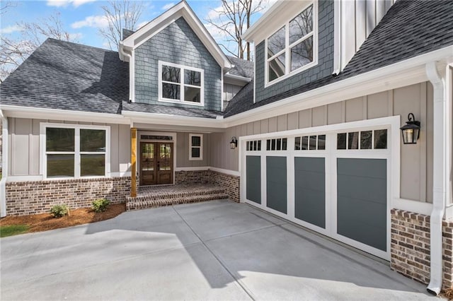 property entrance featuring roof with shingles, brick siding, concrete driveway, french doors, and board and batten siding