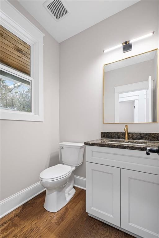 half bathroom featuring vanity, wood finished floors, visible vents, baseboards, and toilet