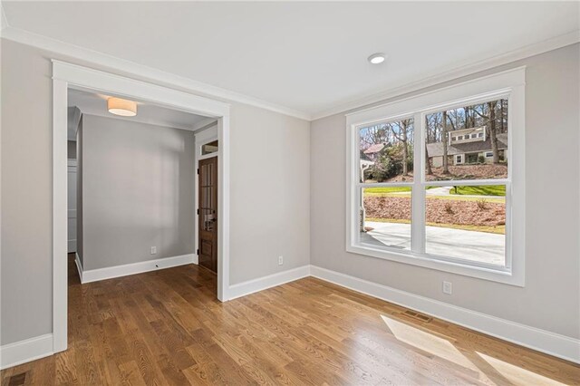 empty room featuring visible vents, baseboards, wood finished floors, and crown molding