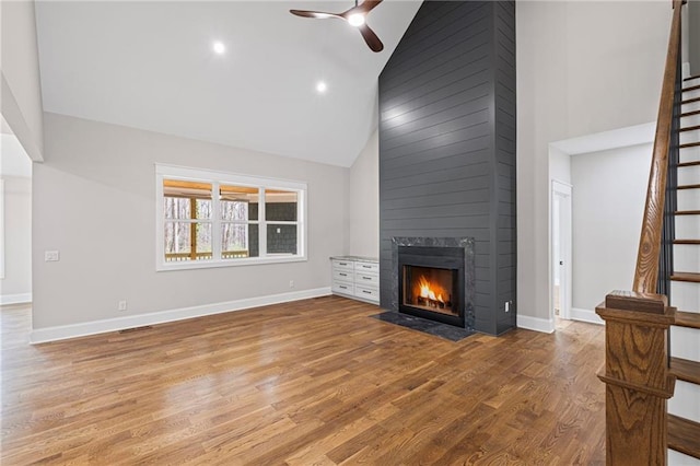 unfurnished living room with a large fireplace, baseboards, ceiling fan, stairway, and wood finished floors