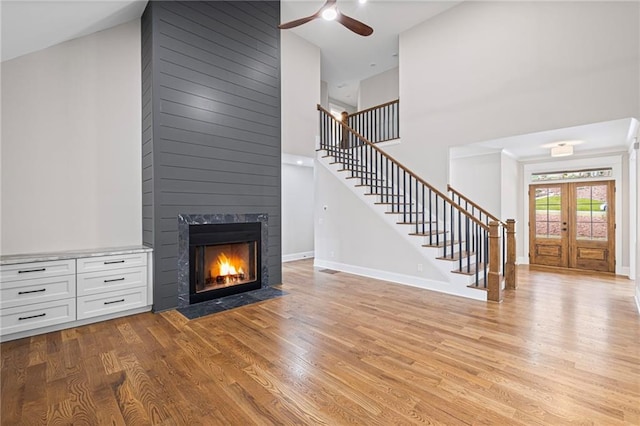 unfurnished living room featuring stairway, a fireplace, a ceiling fan, and light wood finished floors