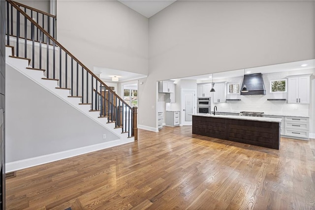 kitchen with baseboards, light countertops, custom range hood, light wood-style flooring, and white cabinetry