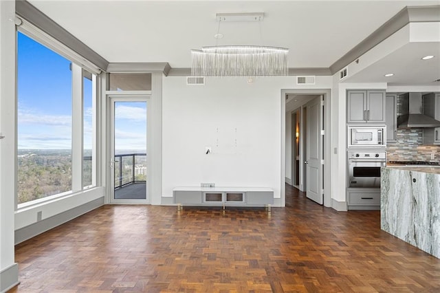 interior space featuring gray cabinetry, built in microwave, stainless steel oven, wall chimney exhaust hood, and decorative backsplash