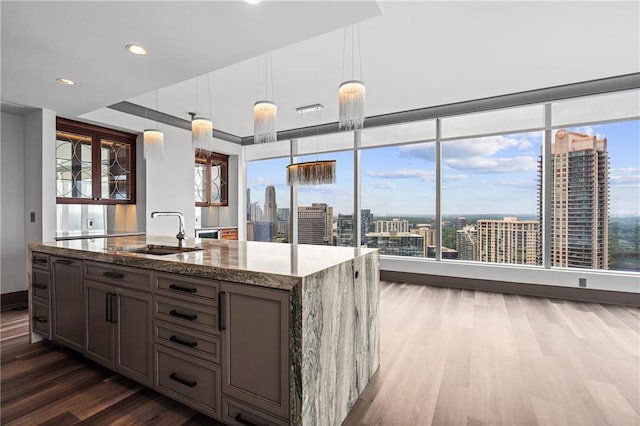 3630 Peachtree Rd NE Unit 2207, Atlanta, GA 30326 - kitchen featuring a sink, wood finished floors, light stone counters, an island with sink, and hanging light fixtures