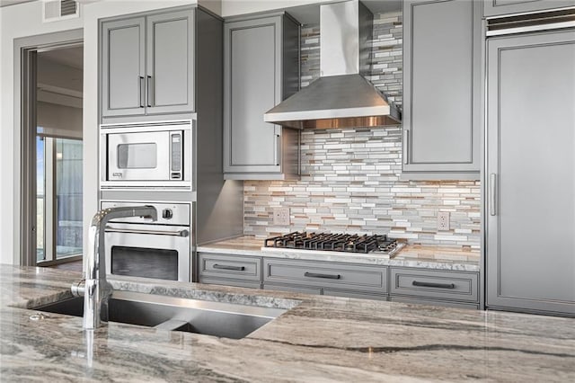 kitchen featuring light stone countertops, sink, stainless steel appliances, wall chimney range hood, and tasteful backsplash